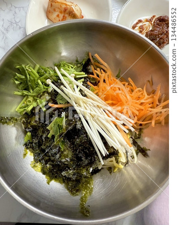 Bibimbap, a vibrant Korean rice dish topped with a variety of seasoned vegetables, gochujang, and a fried egg, often accompanied by sliced meat. Mixed together, it creates a flavorful and balanced. Bibimbap, a vibrant Korean rice dish topped with a variety of seasoned vegetables, gochujang, and a fried egg, often accompanied by sliced meat. Mixed together, it creates a flavorful and balanced. 134486552