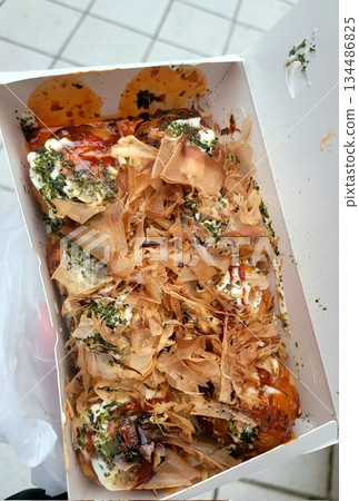 Takoyaki, a popular Japanese street food, are crispy round dough balls filled with octopus, tempura bits, and pickled ginger, topped with takoyaki sauce, bonito flakes, and aonori. 134486825