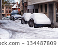 Snow Covered Cars Parked Along Snowy Urban Street With Buildings and Sidewalks 134487809