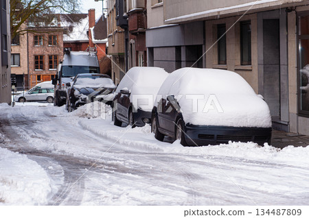 Snow Covered Cars Parked Along Snowy Urban Street With Buildings and Sidewalks 134487809