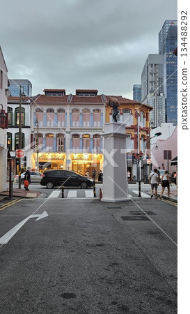 A dynamic statue anchors a lively street scene where pastel shophouses, modern towers 134488292