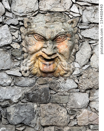 Grotesque stone mascaron carving adorning ancient rock wall 134488440