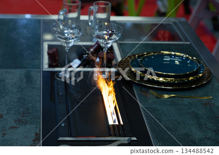 Modern dining table with fire feature and elegant tableware setup Modern dining table with fire feature and elegant tableware setup 134488542