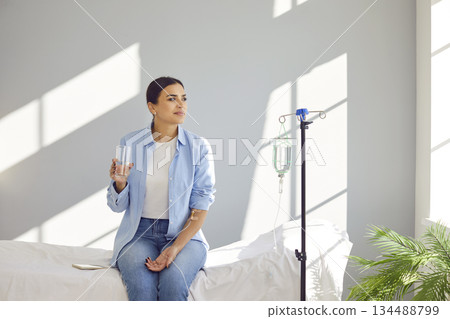 Woman receiving IV drip infusion therapy in her blood sitting in medical clinic with glass of water 134488799