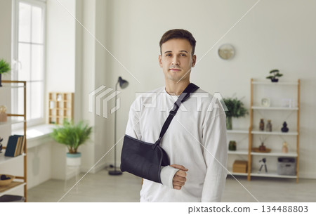 Man standing at home or in hospital on rehabilitation with his arm in plaster cast after injury. 134488803