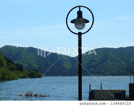 Minimalist street lights on a quiet lakeside, green mountains and blue skies Minimalist street lights on a quiet lakeside, green mountains and blue skies 134489110