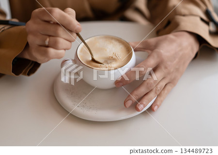 Coffee hands stirring cappuccino in white cup enjoying morning beverage break 134489723