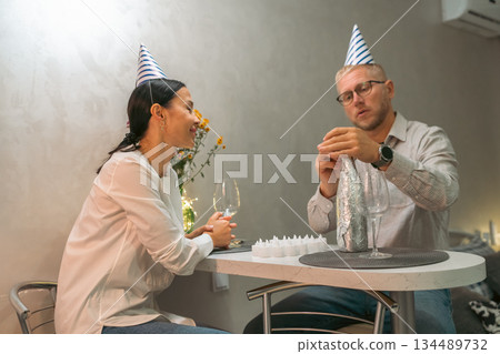 Couple Birthday Party Home Celebration: Indoor intimate birthday celebration; couple wearing party hats; playfully interacting at home. 134489732
