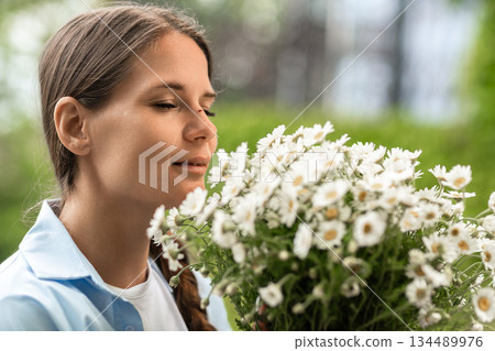 Flowers Woman Portrait, Spring: Smiling girl enjoys daisy bouquet scent in garden during daytime. 134489976