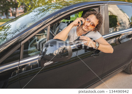 Man with curly hair using phone and looking in the rearview mirror 134490942