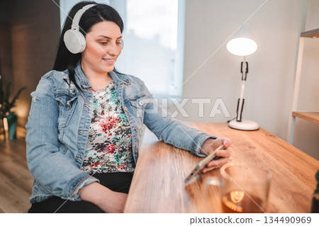 Woman enjoying music and social media on smartphone while working from home 134490969