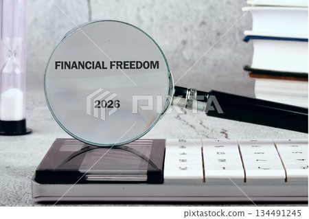 A magnifying glass focuses on Financial Freedom and the year 2026. A calculator, books, and an hourglass are nearby, suggesting financial planning and time management A magnifying glass focuses on Financial Freedom and the year 2026. A calculator, books, and an hourglass are nearby, suggesting financial planning and time management 134491245