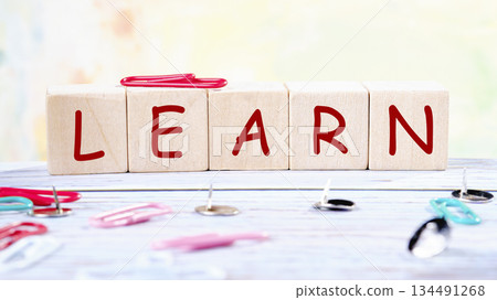 The word LEARN is spelled out with wooden blocks. Colorful paper clips and thumbtacks are scattered around the blocks on a light-colored wooden surface The word LEARN is spelled out with wooden blocks. Colorful paper clips and thumbtacks are scattered around the blocks on a light-colored wooden surface 134491268
