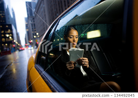 Businesswoman reading on a tablet in a yellow taxi on a rainy city street at night Businesswoman reading on a tablet in a yellow taxi on a rainy city street at night 134492045