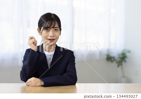 A young female businesswoman in a suit sitting at a desk and smiling A young female businesswoman in a suit sitting at a desk and smiling 134493027