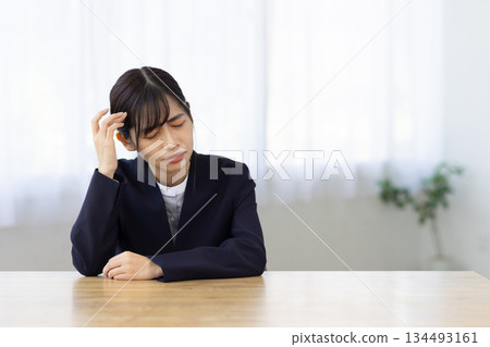 A young woman in a suit holding her head at her desk and worrying A young woman in a suit holding her head at her desk and worrying 134493161
