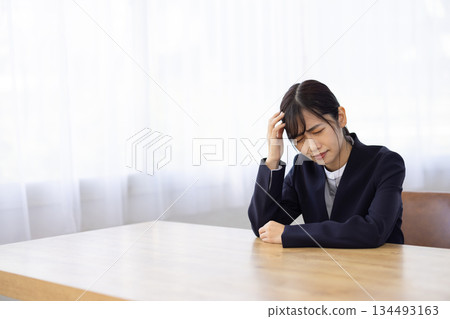 一位身穿西裝的年輕女子在辦公桌前抱著頭，憂心忡忡。 134493163