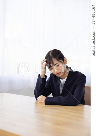 一位身穿西裝的年輕女子在辦公桌前抱著頭，憂心忡忡。 134493164