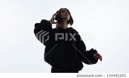 Young woman listening to music with headphones and raised hand against white background. 134493202