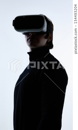 Young man wearing virtual reality headset standing against white background. Young man wearing virtual reality headset standing against white background. 134493204