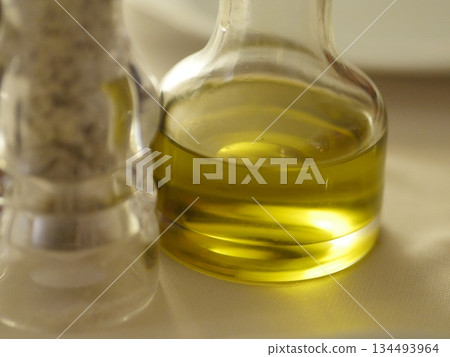 Bottle of olive oil sits on a table next to a salt shaker 134493964