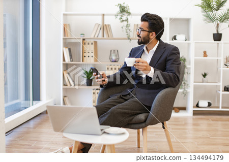 An Arab businessman is taking a break with a cup of coffee while looking out the window An Arab businessman is taking a break with a cup of coffee while looking out the window 134494179