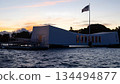 USS Arizona Memorial Pearl Harbor Honolulu Hawaii sunset view with American flag, historic WWII monument silhouette on ocean water, solemn patriotic dusk scene. 134494877