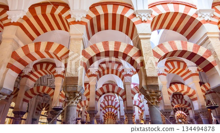 Interior of Mosque-Cathedral of Cordoba Spain featuring iconic red and white striped Moorish arches, ancient stone columns and historic Islamic architecture inside the famous Mezquita landmark. Interior of Mosque-Cathedral of Cordoba Spain featuring iconic red and white striped Moorish arches, ancient stone columns and historic Islamic architecture inside the famous Mezquita landmark. 134494878