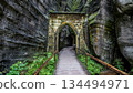 Historic Gothic Gate entrance in Adrspach-Teplice Rocks Czechia with wooden walkway between massive mossy sandstone cliffs in famous Bohemian rock city nature reserve. 134494971