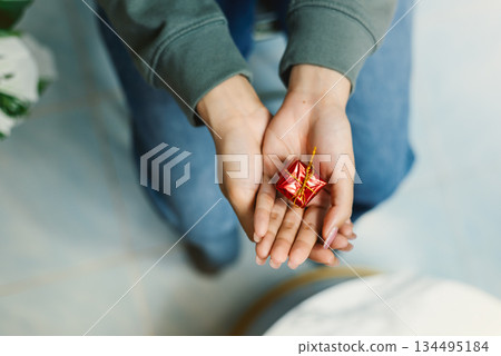 Top view of hand holding small red gift box with gold ribbon 134495184