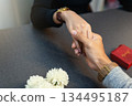 Close up of couple holding hands with red jewelry ring box and flowers 134495187