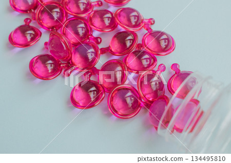 Vibrant pink hair serum capsules spilling from a plastic bottle, for dry, damaged and frizzy hair. Close-up on a light blue background Vibrant pink hair serum capsules spilling from a plastic bottle, for dry, damaged and frizzy hair. Close-up on a light blue background 134495810
