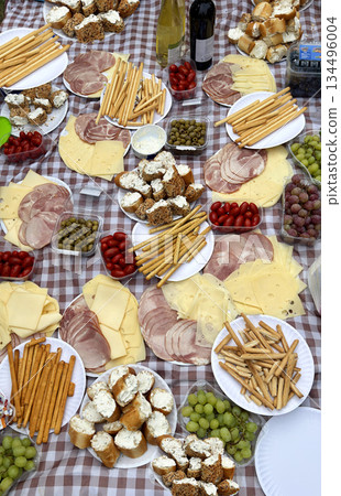 Snack for tourists along the trail. Cured meat platter, cheese, breadsticks grissini, bruschetta canapes with cream cheese, grapes, olives, cherry tomatoes, wine. Carpathian mountains, Romania 134496004