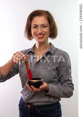 A woman smiles and holds a Tibetan bowl for meditative practices. A woman smiles and holds a Tibetan bowl for meditative practices. 134496082