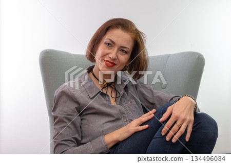 A woman is sitting in a chair in a relaxed pose and smiling. A woman is sitting in a chair in a relaxed pose and smiling. 134496084