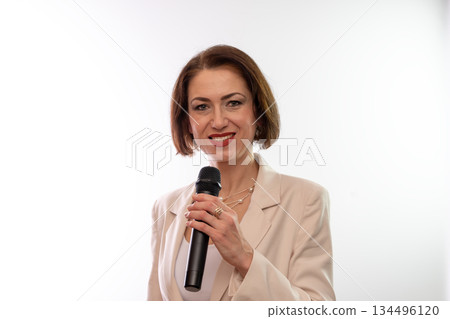 A smiling woman holds a microphone and looks at the camera on a studio white background. 134496120