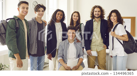 Teacher standing with high school students and looking cheerful at camera in the classroom. Teacher standing with high school students and looking cheerful at camera in the classroom. 134496365