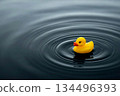 Yellow rubber duck toy floating on dark water creating ripples 134496393