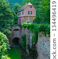 A historic pink stone building stands prominently above a stone bridge and ivy-covered walls in a lush forest. This serene architectural shot is ideal for travel guides and history projects. 134496419