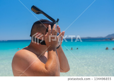 Man adjusting snorkeling mask near the sea before swimming. Active beach leisure and summer vacation concept, Sardinian, La Maddalena, Italy Man adjusting snorkeling mask near the sea before swimming. Active beach leisure and summer vacation concept, Sardinian, La Maddalena, Italy 134496855