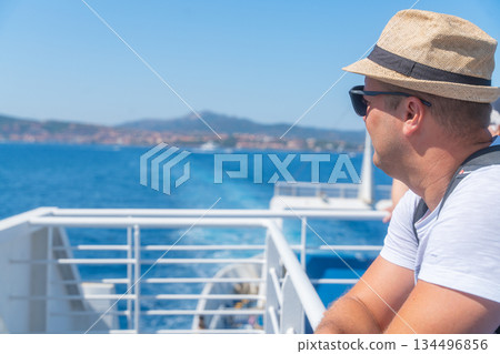 Man standing on ferry deck during sea crossing, looking at the horizon. Summer travel, maritime transport and journey concept 134496856