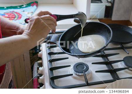 the dough spreads in a pan for baking pancakes in the hands of an elderly woman the dough spreads in a pan for baking pancakes in the hands of an elderly woman 134496894