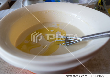 the finished pancake batter with oil in a white bowl with a metal whisk 134496895