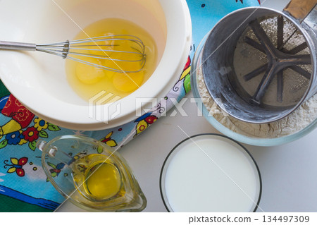 raw ingredients for pancakes are laid out on a multi-colored tablecloth and white background 134497309