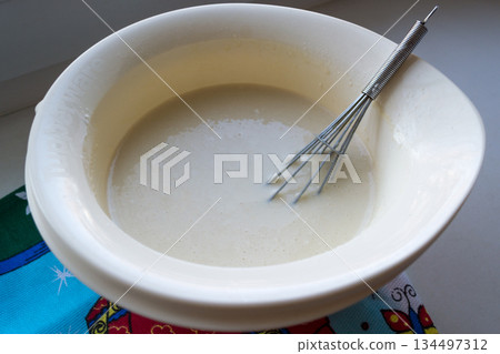 the finished pancake batter in a white bowl with a metal whisk the finished pancake batter in a white bowl with a metal whisk 134497312