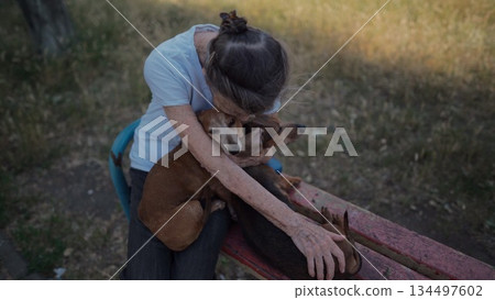 Happy senior woman holds a small dachshund dog in her arms, smiles hugs, presses and shows love to her pet on a bench in the park. Female 90 years old spends time with her best friend pet on street 134497602