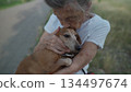 Happy senior woman holds a small dachshund dog in her arms, smiles hugs, presses and shows love to her pet on a bench in the park. Female 90 years old spends time with her best friend pet on street 134497674