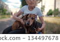 Animal theme is a lonely old woman best friend. Caucasian 90 years old senior female is happy to spend time with her pet small dachshund dog, holding her in her arms, hugging hugs and kisses outdoor 134497678