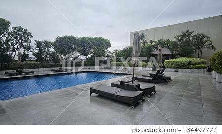A serene poolside with wicker loungers, closed umbrellas A serene poolside with wicker loungers, closed umbrellas 134497772