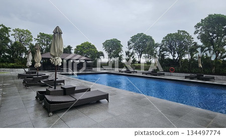A serene poolside with wicker loungers, closed umbrellas A serene poolside with wicker loungers, closed umbrellas 134497774